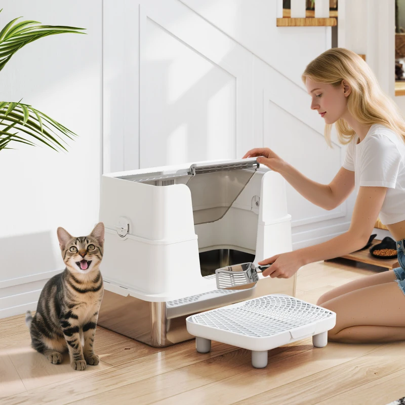 Woman cleaning stainless steel litter box while cat sits nearby.