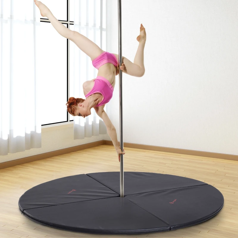 Woman performing pole dance move on black circular mat in studio.