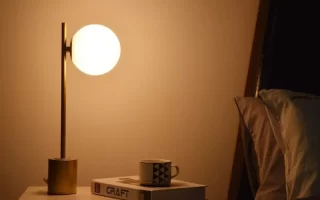 Warm bedside lamp glowing beside books and coffee cup on nightstand.