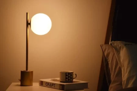Warm bedside lamp glowing beside books and coffee cup on nightstand.