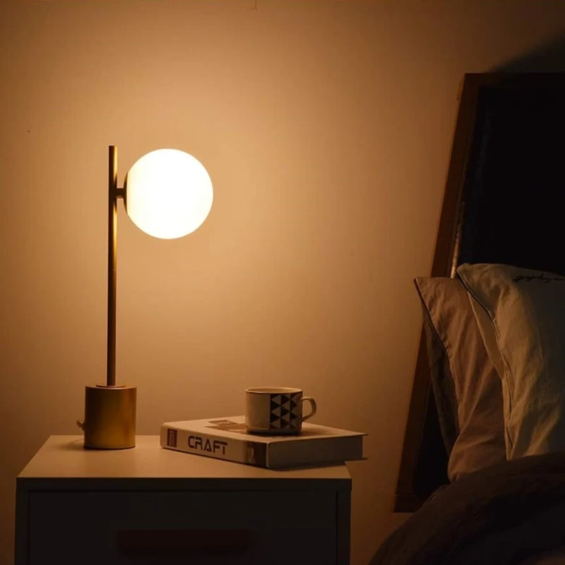 Warm bedside lamp glowing beside books and coffee cup on nightstand.