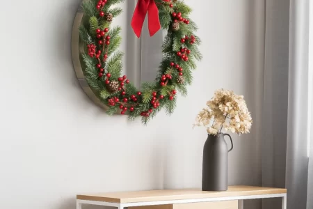 Round wall mirror decorated with a classic Christmas wreath featuring red berries, pinecones, and a red bow.