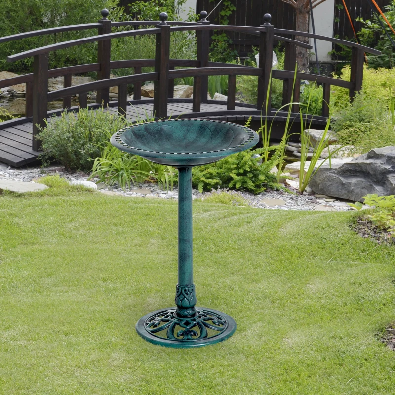 Green pedestal bird bath standing on level grass in a landscaped backyard.