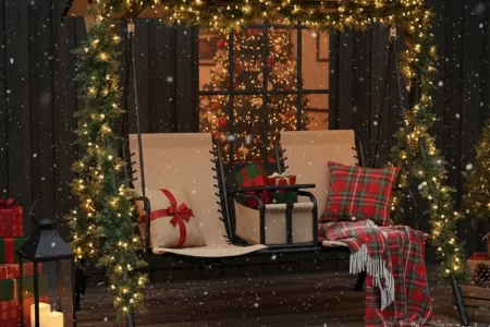 Christmas porch swing with garland, gifts, pillows, and lantern