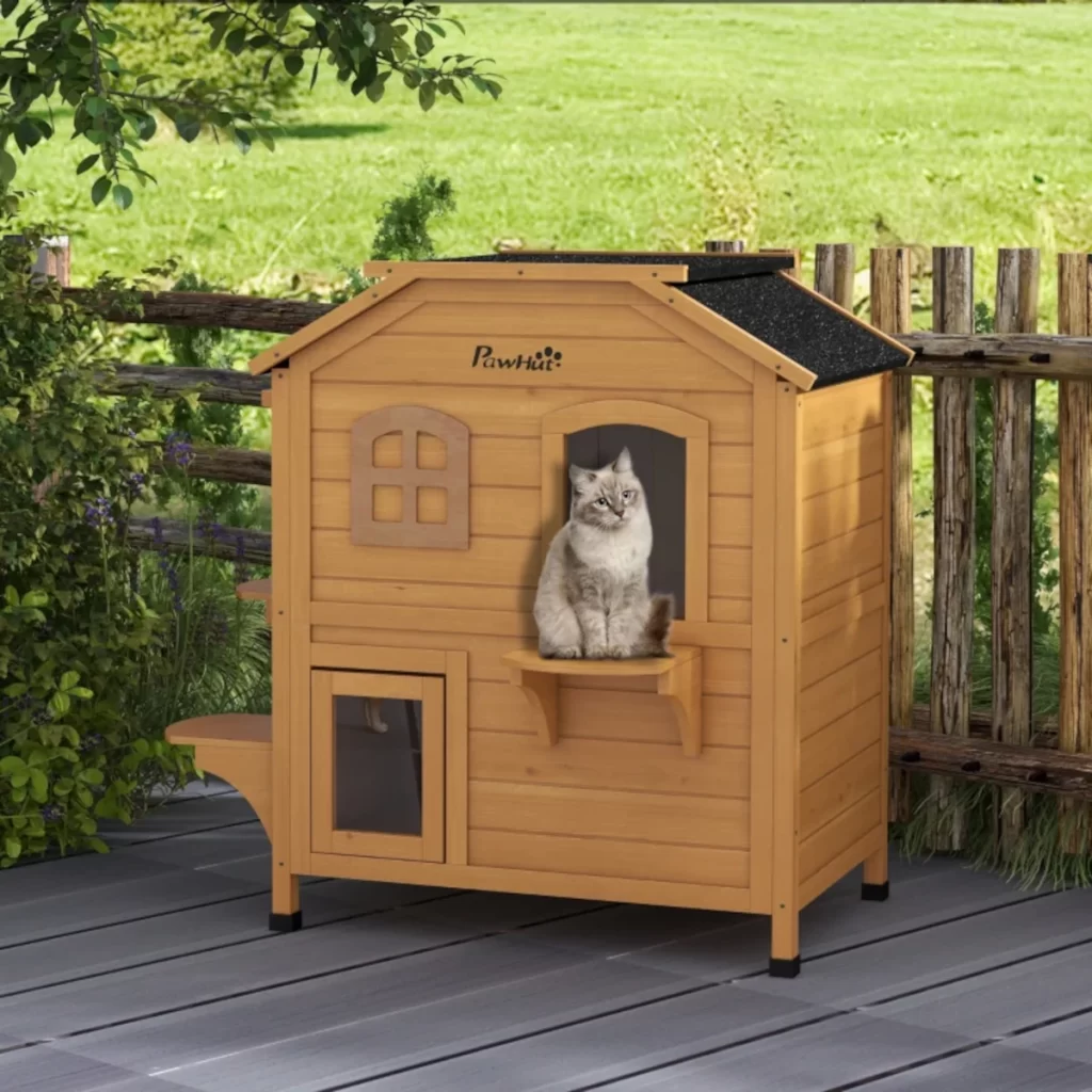 Two cats sitting on wooden outdoor cat house platforms with a multi-level design and windows.