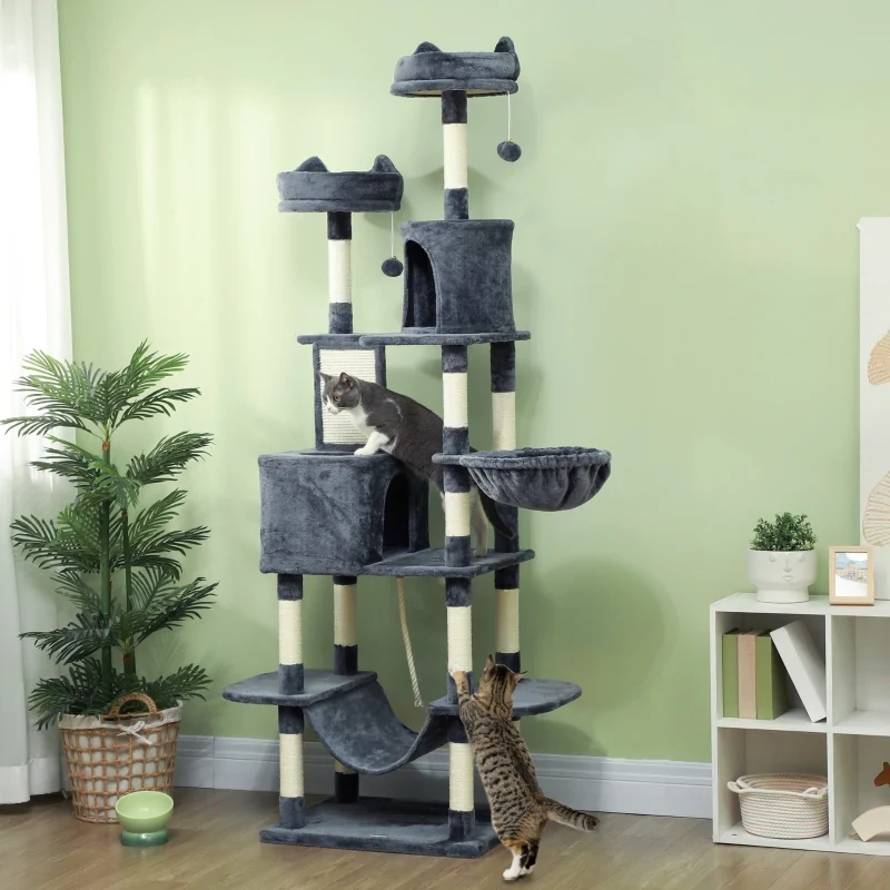 Two cats climbing and resting on a tall grey cat tree placed in a living room corner.
