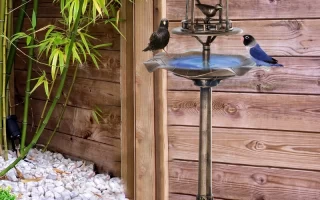 Green decorative bird bath standing on lawn near a garden bridge and landscaped plants.